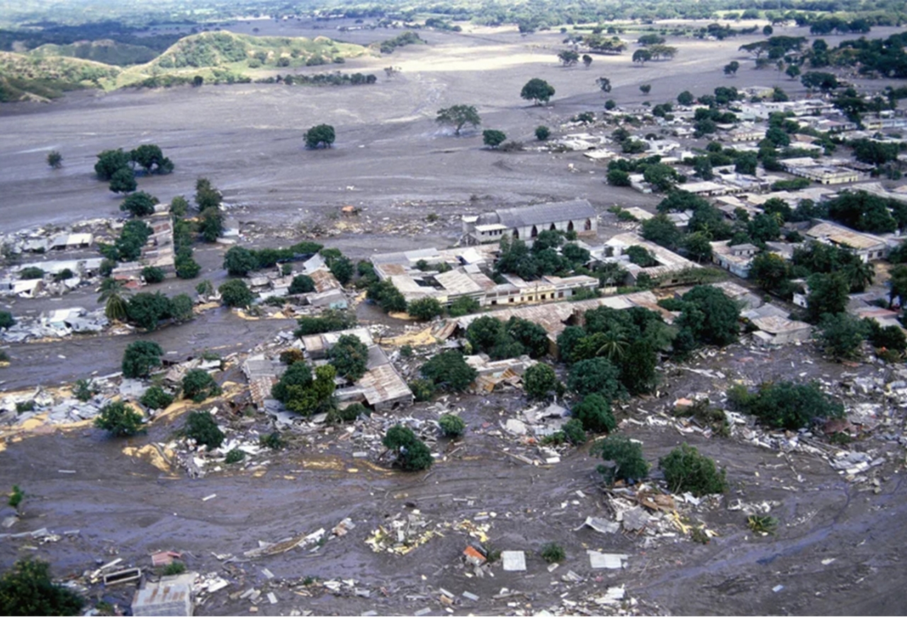 Fotografía aérea de Armero luego de la erupción del Nevado del Ruiz|Diego Arake (izquierda) junto a un amigo, cuando ambos eran menores de edad. Fotografía de la época en que Diego estuvo presente como rescatista en Armero|||