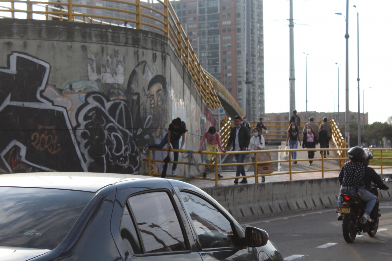 Familia con dos menores escala por la baranda del puente mientras carios vehículos se movilizan a su lado.|Niña pasa por encima de la baranda con el riesgo de caer hacia el camino vehicular.|Hombre verifica que un menor pase por encima de la baranda.|Dos hombres pasando por encima de la baranda.|Luego de saltar la baranda, los hombres bajan de las instalaciones del puente evadiendo las indicaciones peatonales y obstruyendo el corredor vehicular.|Mujer intenta saltar sobre la baranda mientras uno de sus pies se encuentra apoyado en el borde del separador vial.|||