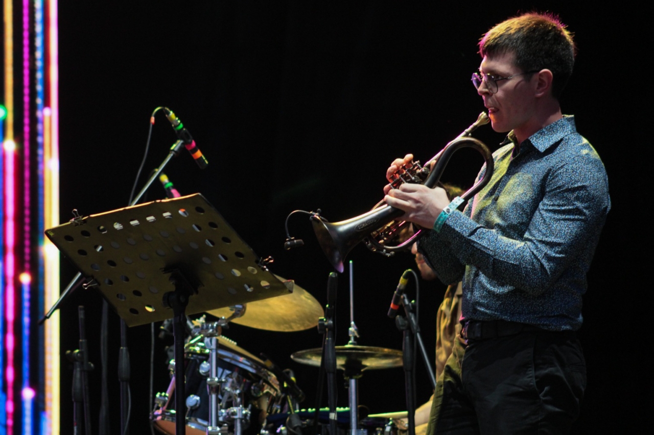 El trompetista preparandose para entrar a la canción|Antonio Arnedo tocando el saxofon, uno de los instrumentos más emblemetaicos de este género|El tempo de la música orquestado por la batería|El piano uno de los instrumentos que le dio raiz a este género|El contrabajo y la guitara electrica como una fusión de cuerdas en la canción|Los bogotanos disfrutando del show|Camila Bañados un artista chilena influyente de este género|Un violin y un contrabajo acompañando la voz de Camila Bañados|Performace de moldear la música a través de la arcilla|El público bogotano de todas las edades|La colombiana Gabrilela Ponce como artista invitada de Camila Bañados|||