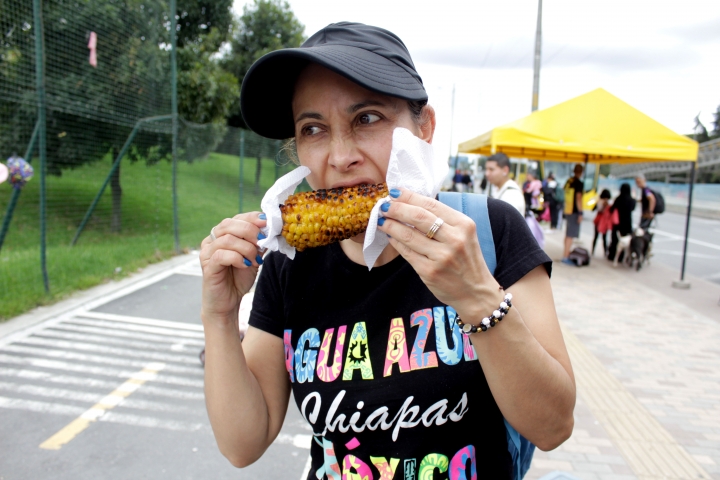 Persona degustando de una mazorca asada, en un puesto callejero por la av 68